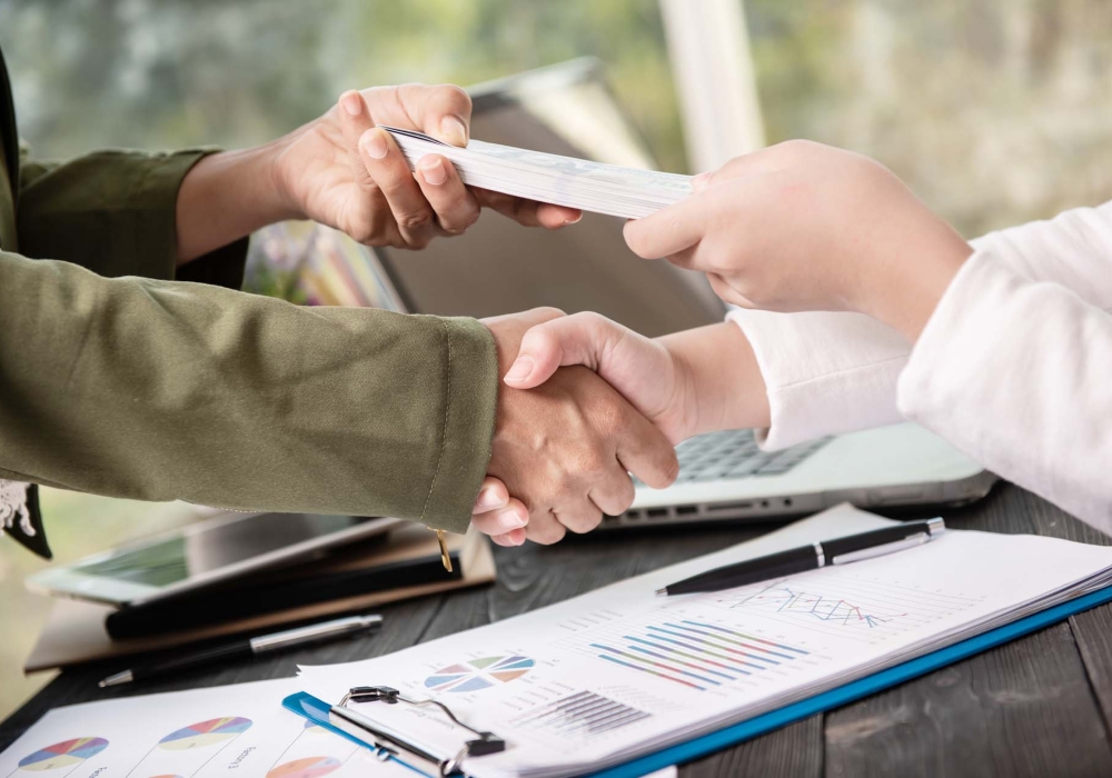 Business people shaking hands, finishing up meeting. businessman giving money to his partner while making contract - bribery and corruption concepts.