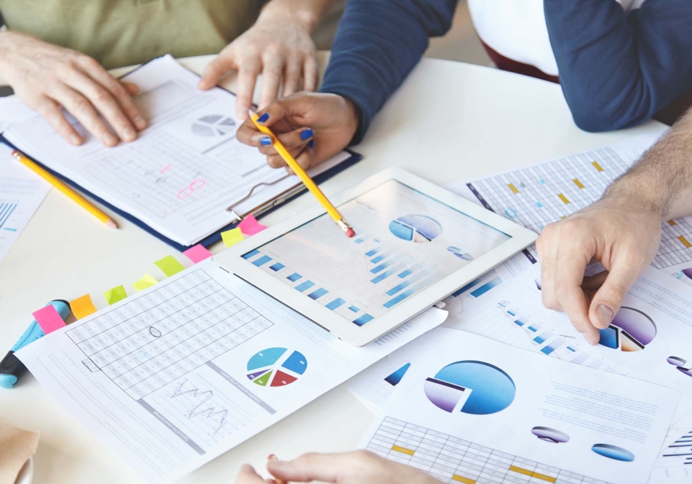 Cropped shot of people of diverse races working on business plan, analyzing value of goods, services, growth rate, making review of market situation, counting loss, using modern devices and touch pad